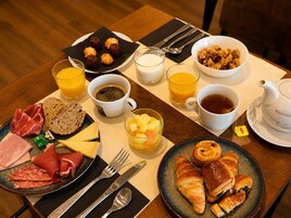 Una mesa de desayuno con diversos alimentos, como carnes, queso, croissants y fruta.