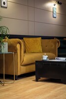 Una sala de estar moderna con un sofá color mostaza, una mesa de centro negra y una mesita auxiliar con una planta.