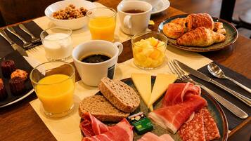 A breakfast setting with croissants, cheese, ham, and a fruit bowl.