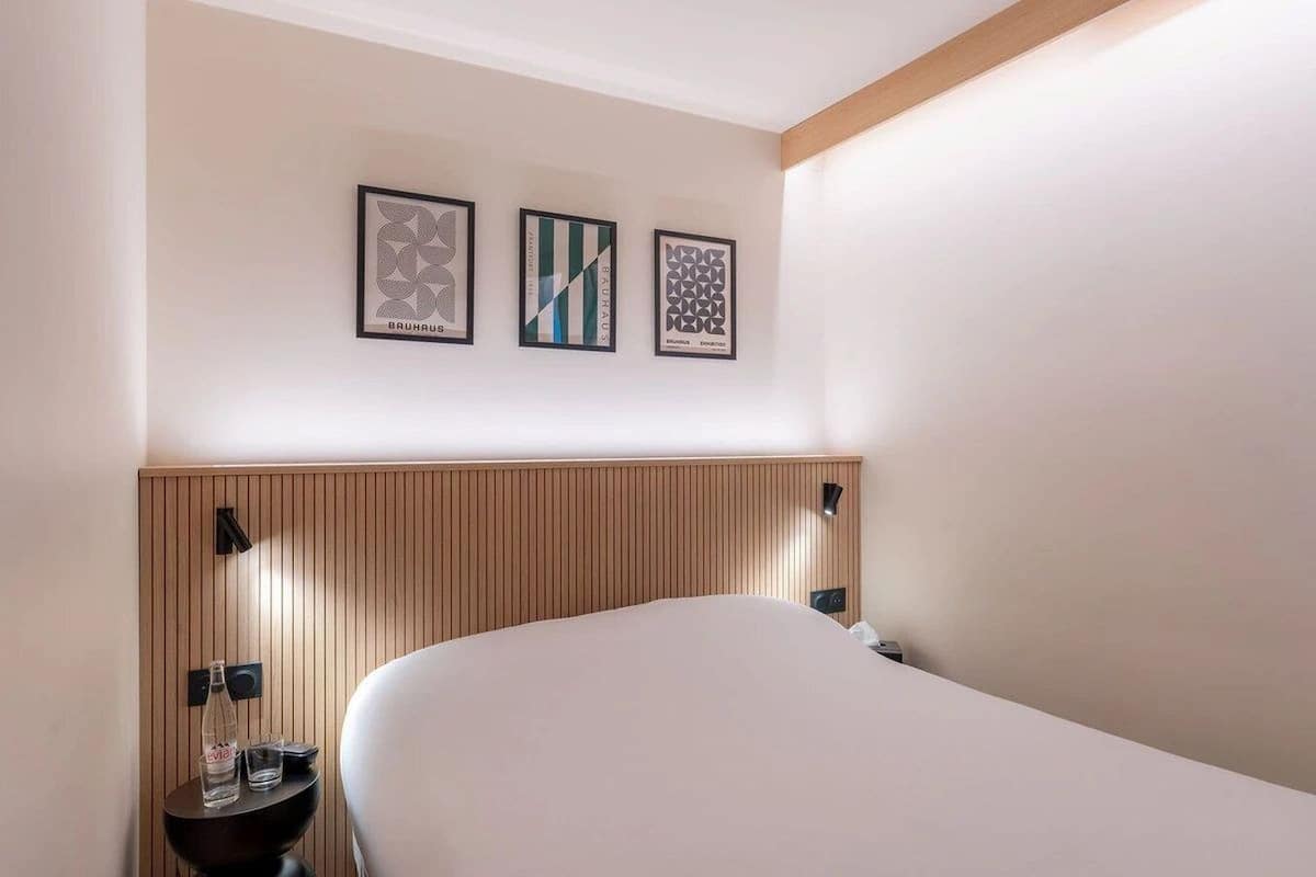 Een hotelkamer met een groot bed, een houten hoofdeinde en drie ingelijste kunstwerken aan de muur.