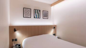 A hotel room with a large bed, a wooden headboard, and three framed artworks on the wall.