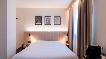 Una habitación de hotel con una cama grande, un cabecero con líneas verticales, dos mesitas de noche con lámparas, una cafetera y una obra de arte enmarcada sobre la cama.