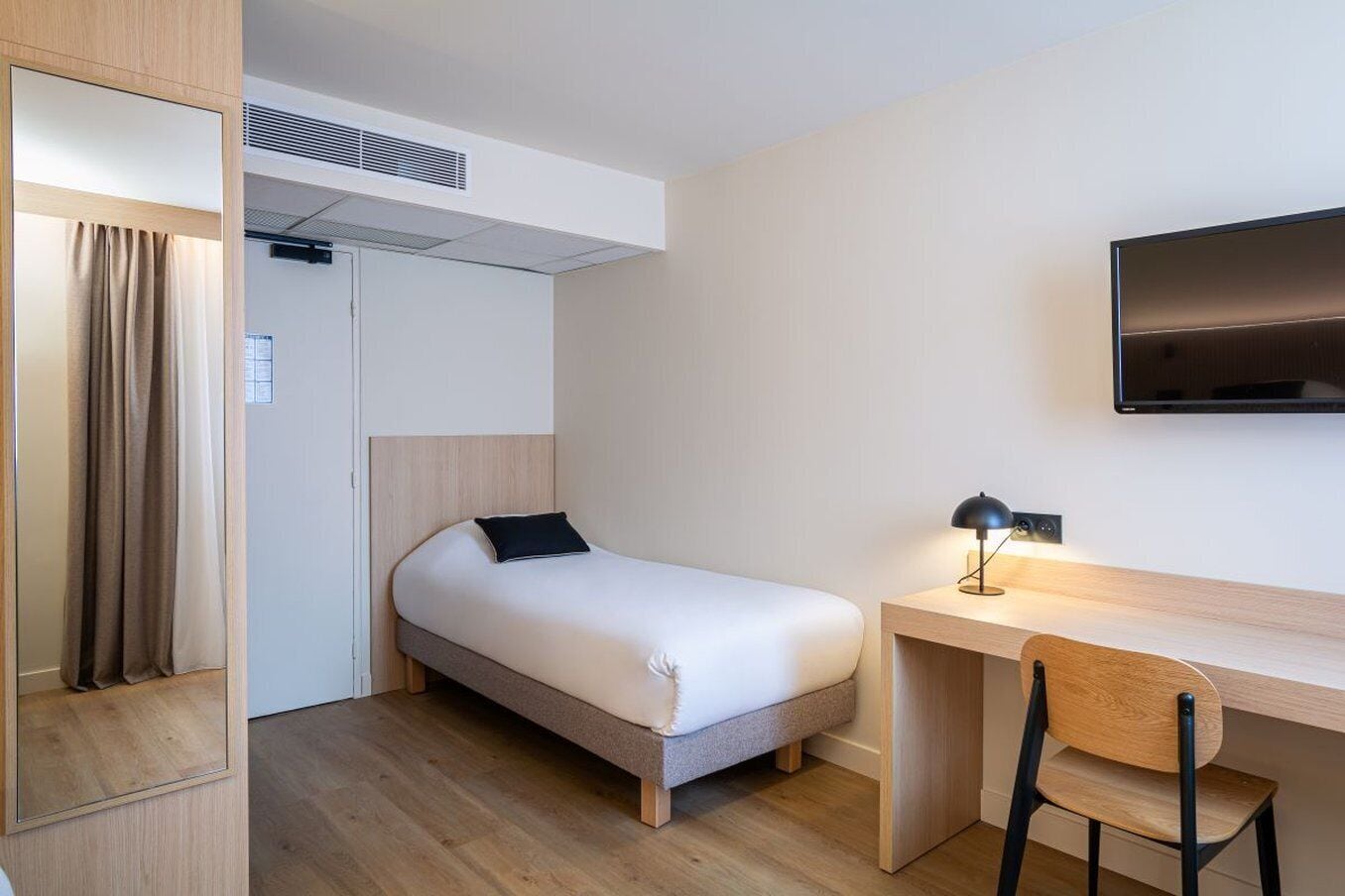 Une chambre d’hôtel de taille réduite, comprenant un lit simple, un bureau et une chaise.