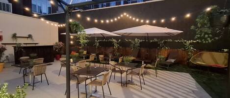 An outdoor patio area with tables and chairs, string lights, and potted plants.