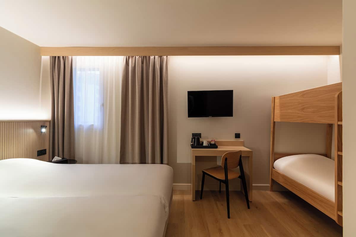 Een hotelkamer met een groot bed, een bureau met een stoel, een televisie en een stapelbed.