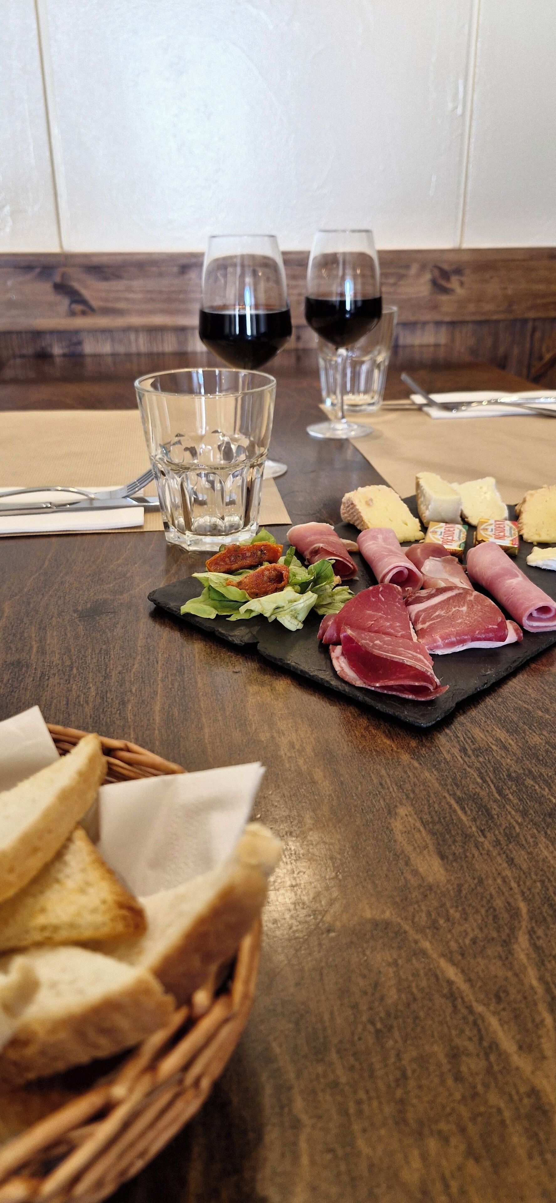 A dining table with a variety of meats, cheeses, and bread, along with two glasses of red wine.