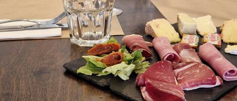 A dining table with a variety of meats, cheeses, and bread, along with two glasses of red wine.