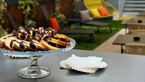 A dessert platter on a table with a glass stand, a white napkin, and an outdoor seating area with a yellow chair and a white umbrella. - Grand Hôtel de la Seine (Rouen)
