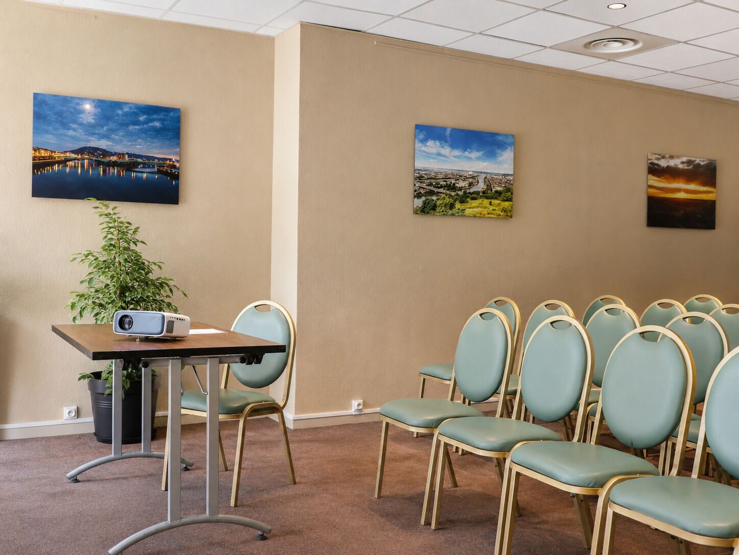 A conference room with a projector, a table, and a row of chairs. There are three paintings on the walls.