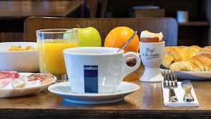 A breakfast table with a plate of cereal, a glass of orange juice, a croissant, and a cup of coffee. - Grand Hôtel de la Seine (Rouen)