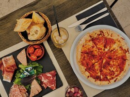 Una mesa con pizza, pan, un vaso de bebida y una variedad de carnes y quesos.