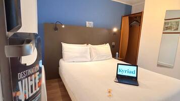 Quarto de hotel com cama, um laptop sobre a cama, um cartaz na parede e piso de madeira.