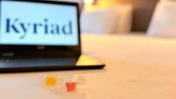 A laptop with the word "Kyriad" on its screen, a bed with white bedding, and a small bowl of fruit on the bed.