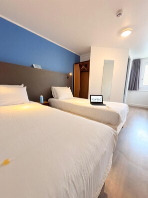 A hotel room with two beds, a wardrobe, a bedside table, a nightstand, a framed sign, and a window with curtains. - Kyriad Blois Sud-Vineuil (Vineuil)