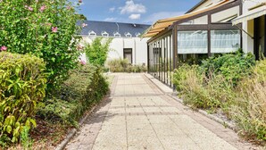 A pathway leading to a building with a covered outdoor area and a garden with flowering plants. - Kyriad Blois Sud-Vineuil (Vineuil)