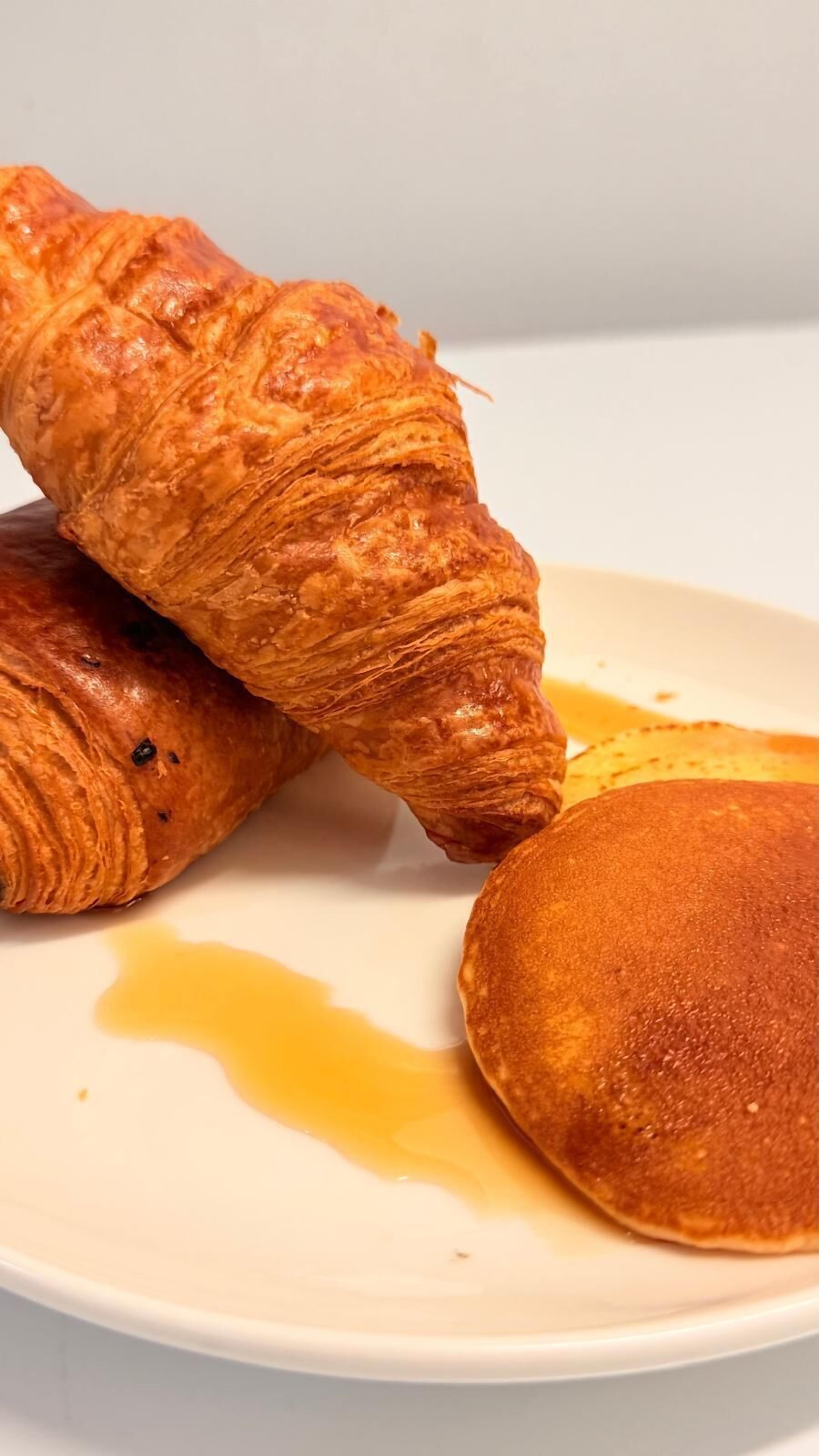 A plate with a croissant and a pancake with syrup.