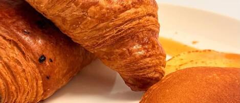 A plate with a croissant and a pancake with syrup.