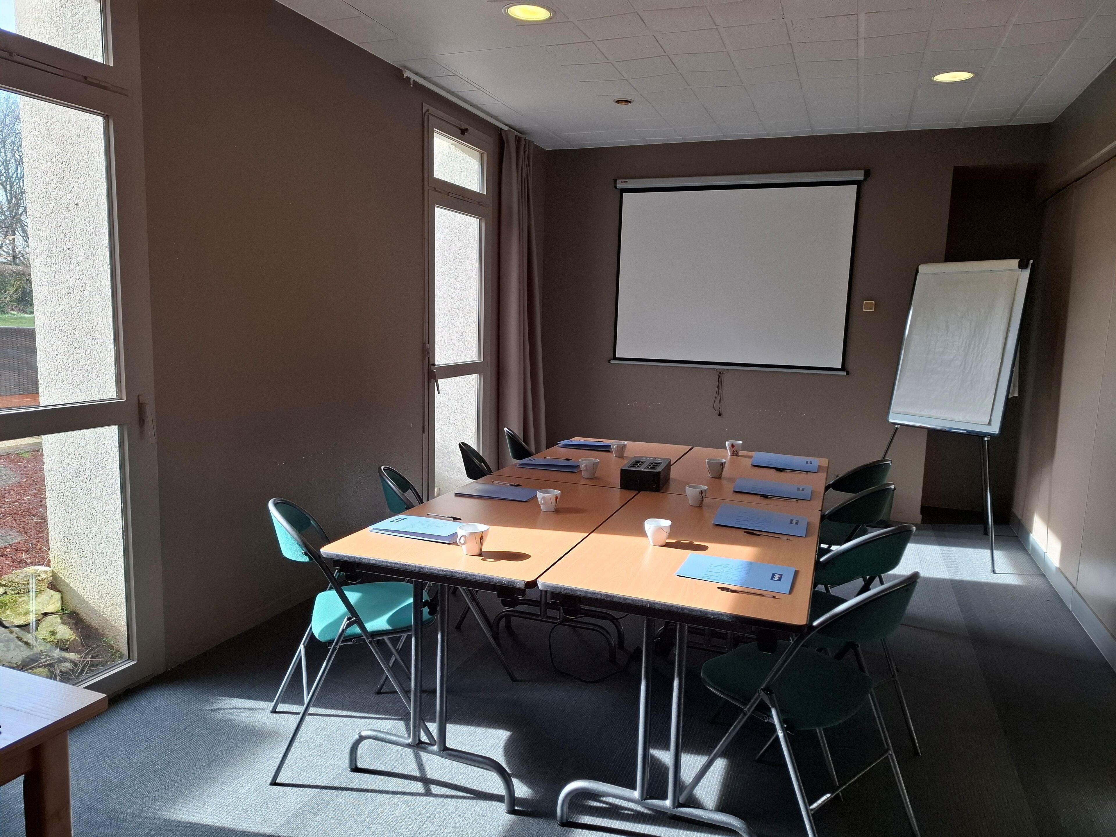 Un salón de conferencias con una larga mesa, sillas, una pantalla de proyector y una pizarra.
