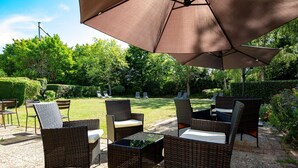 An outdoor patio with wicker furniture, a large umbrella, and a well-maintained garden. - Kyriad Blois Sud-Vineuil (Vineuil)