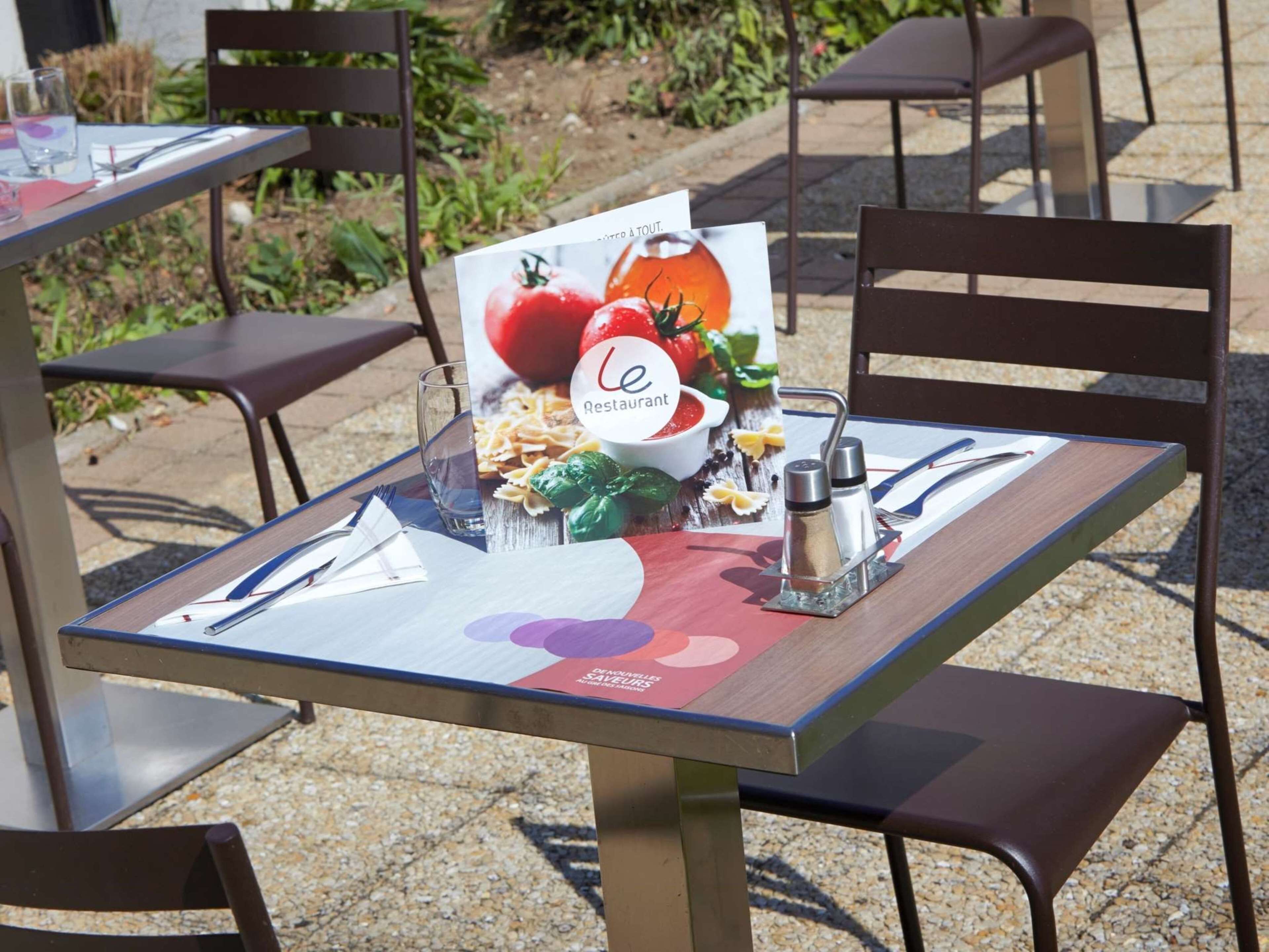 An outdoor dining table with a menu, cutlery, and condiments.