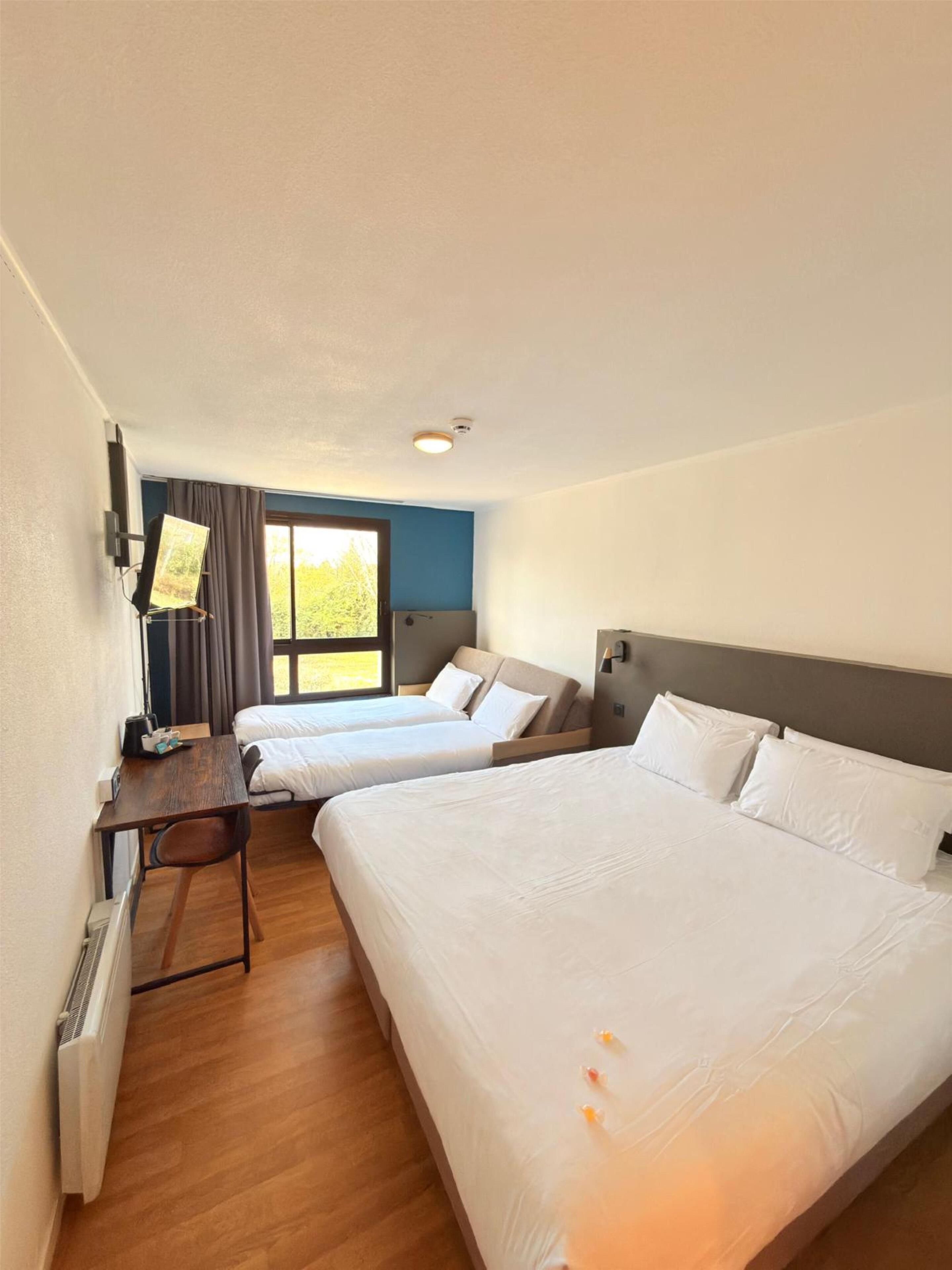 A hotel room with two beds, a desk, and a window with curtains.