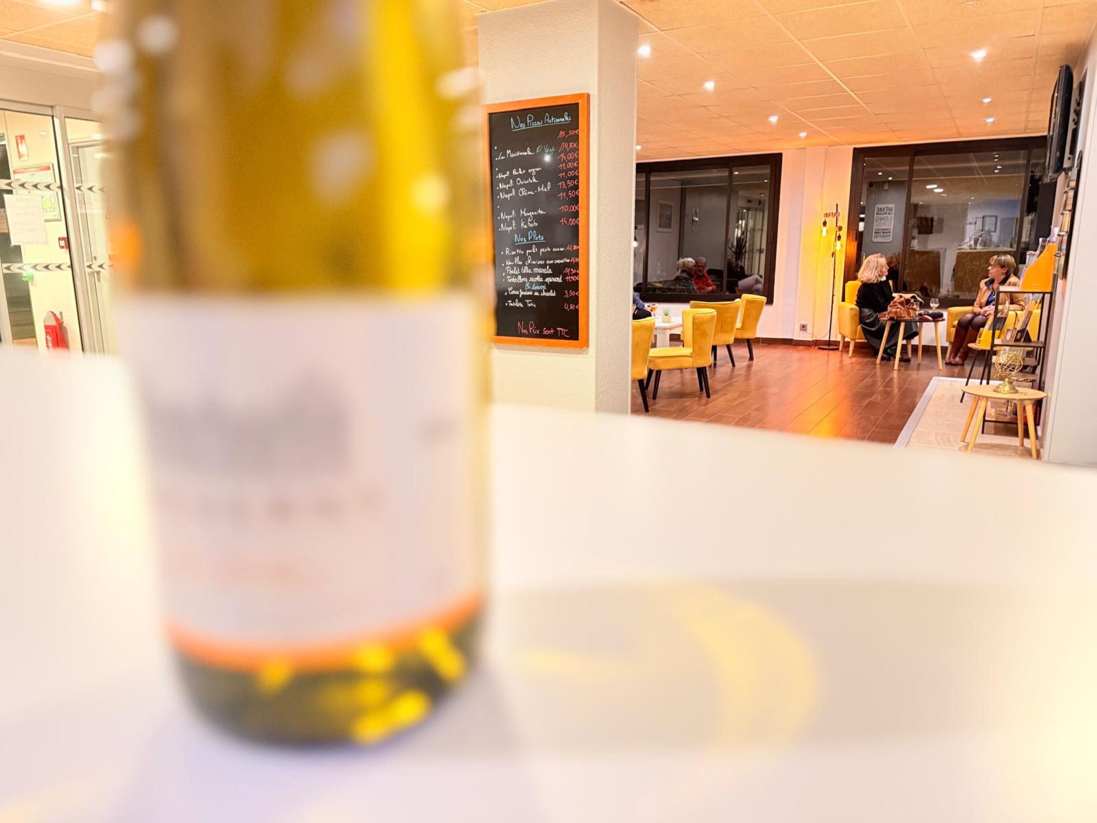 Ein Restaurantinnenraum mit einer Speisekarte, gelben Stühlen und einem Tisch mit einer Weinflasche.