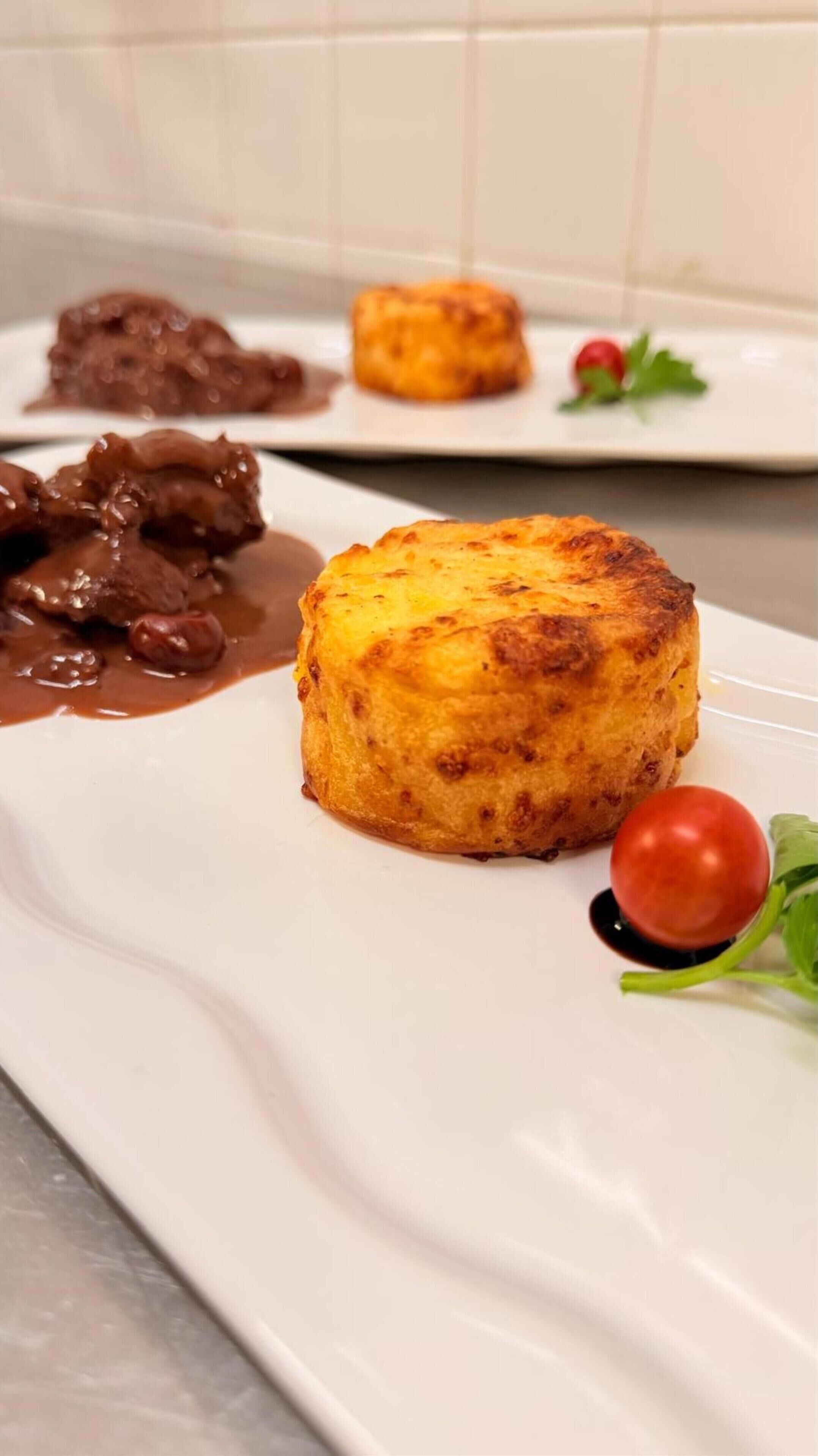 A dessert plate with a golden-brown baked item, a sauce, and a cherry tomato.