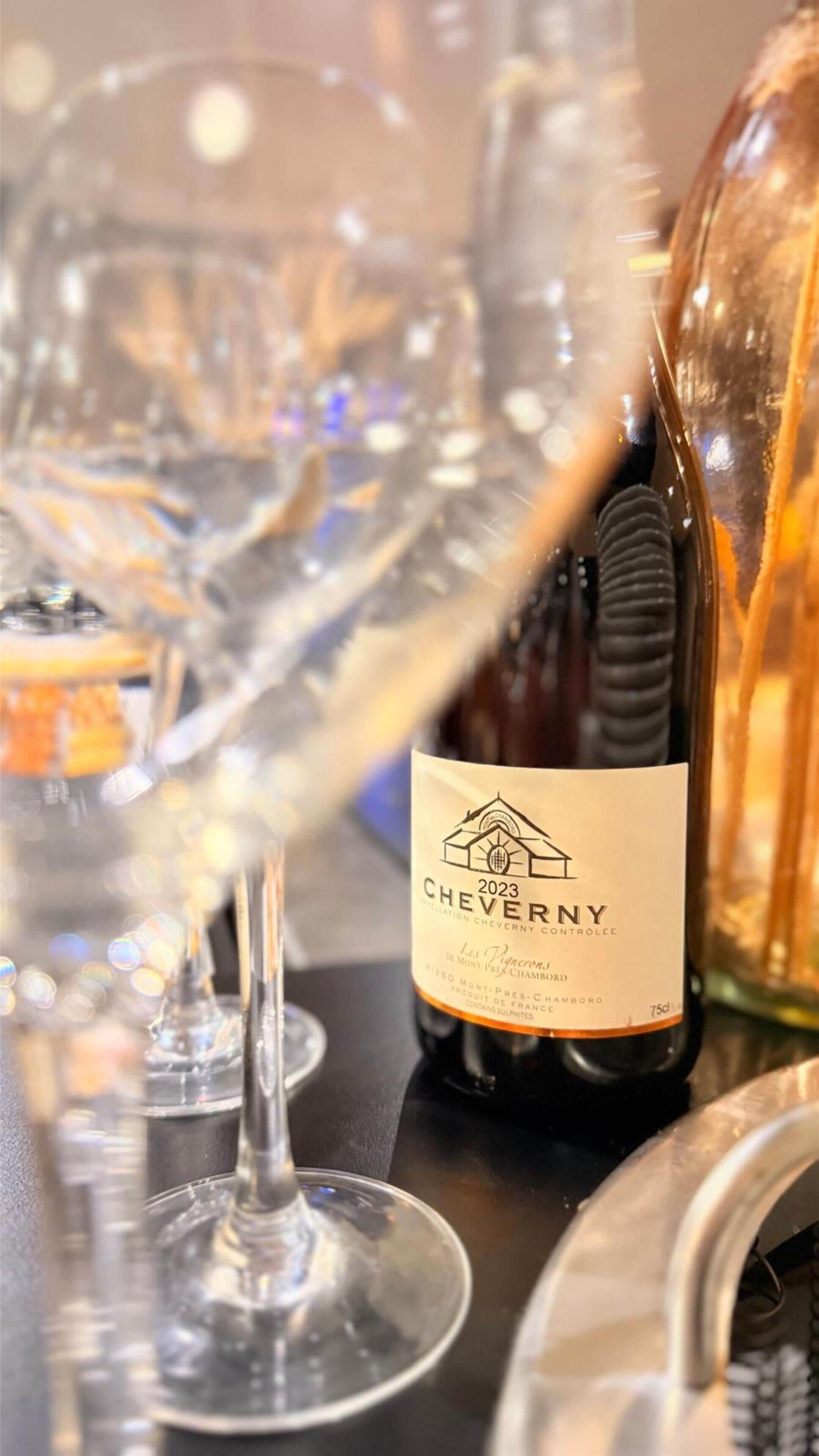 Une bouteille de vin de Cheverny, millésime 2023, avec son étiquette, est posée sur une table, entourée de plusieurs verres à vin.