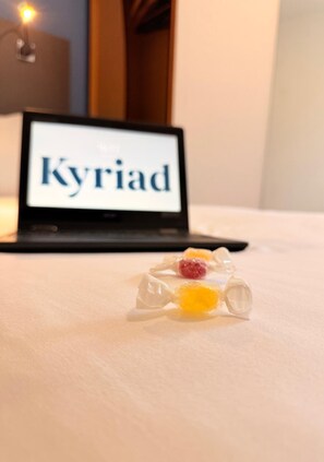A laptop with the text "Kyriad" on its screen, a bed with a white sheet, and a clear plastic bag with candies on it. - Kyriad Blois Sud-Vineuil (Vineuil)