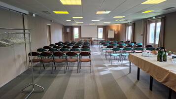 A conference room with rows of chairs, a long table with bottles and glasses, and a projector screen.
