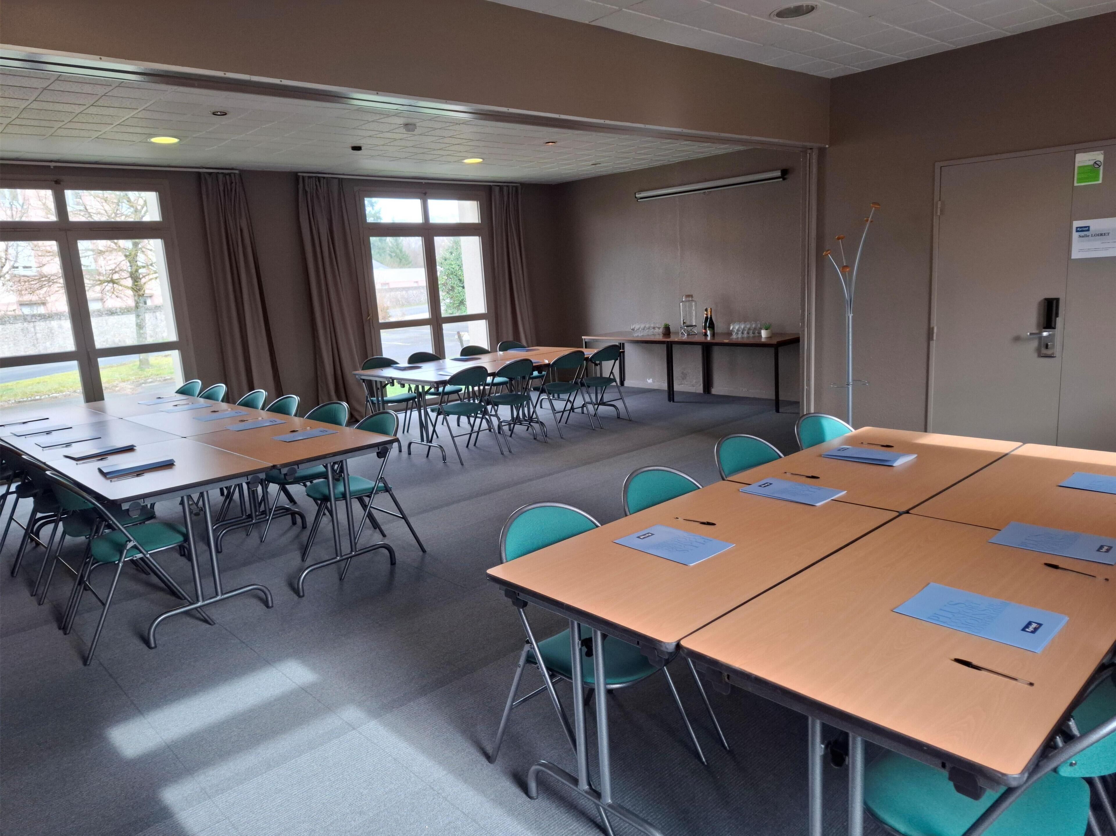 A conference room with multiple tables and chairs, large windows, and a door with a sign.