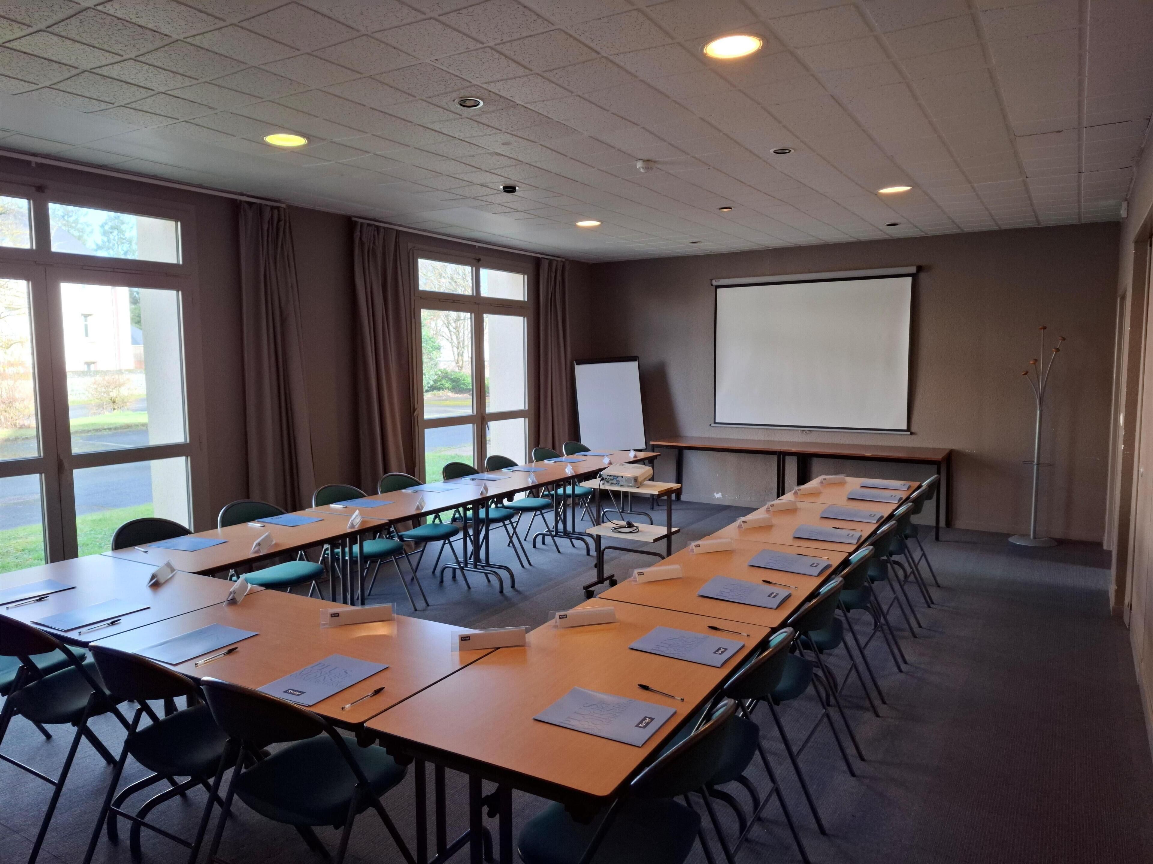 A conference room with a long table, chairs, a projector screen, and a whiteboard.