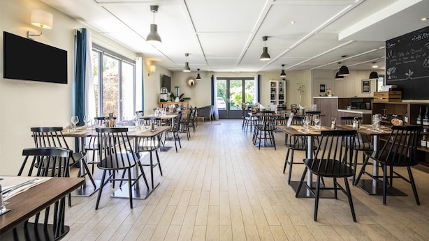 Un restaurant spacieux avec de nombreuses tables et chaises, un téléviseur à écran plat fixé au mur et un tableau noir affichant le menu, situé sur le côté droit.