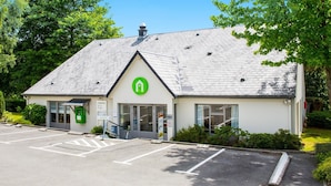 Un bâtiment orné d’un logo vert, un parking et un jardin bien entretenu.