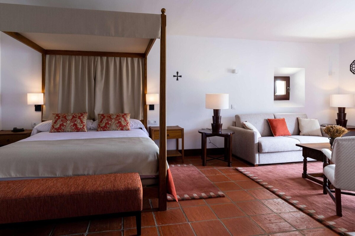 A hotel room with a four-poster bed, a sofa, a chair, and a small table.
