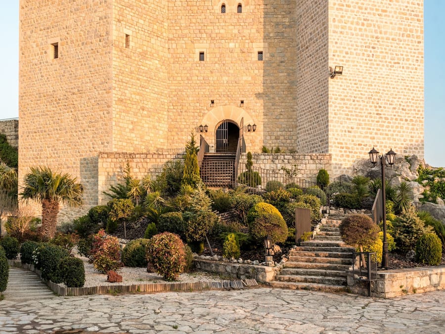 Un edificio de piedra histórico con una entrada central, rodeado de un jardín ajardinado y un camino adoquinado.