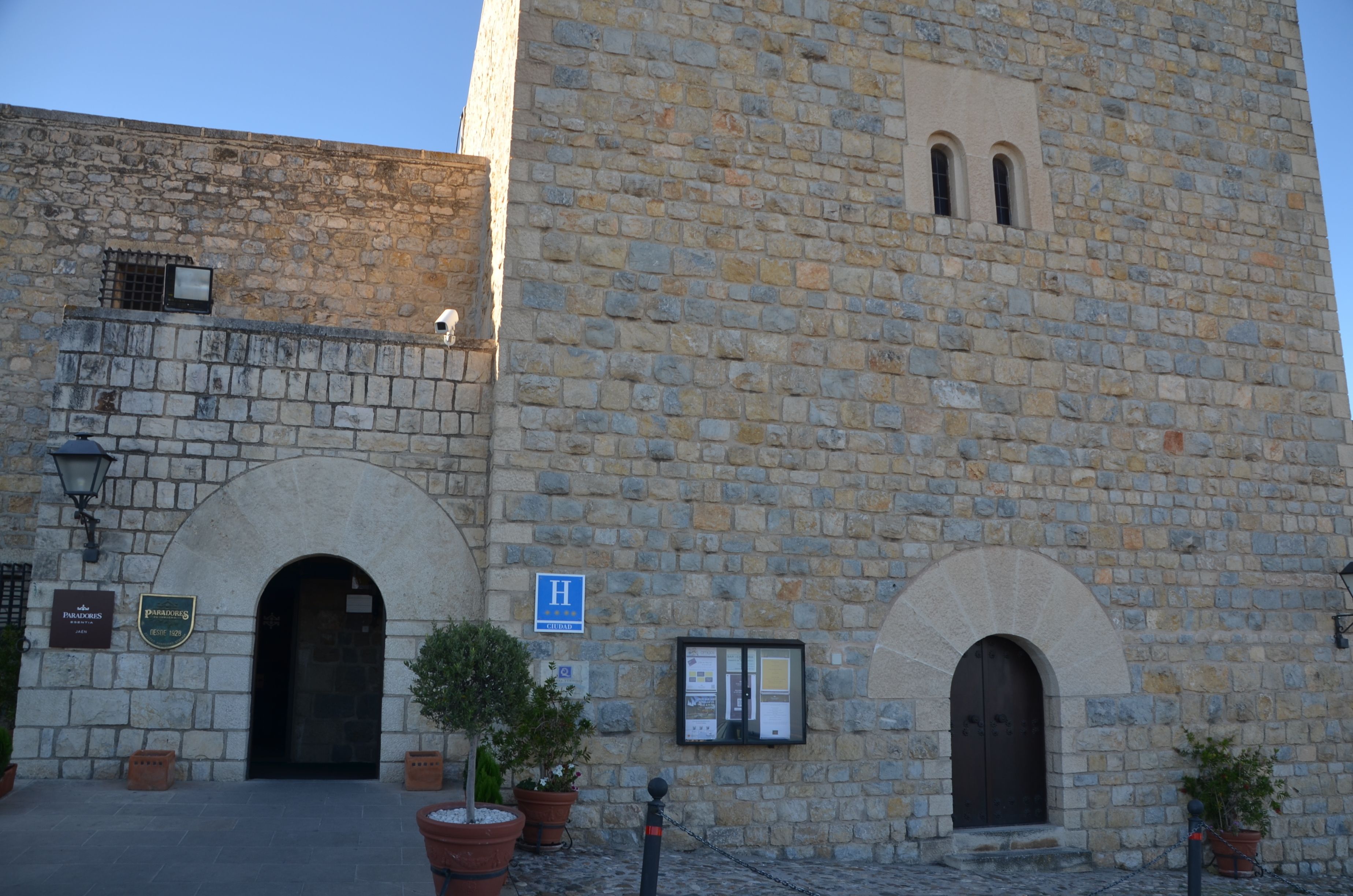 Un edificio de piedra con un gran arco de entrada, un ventanal arqueado más pequeño y un letrero que indica un hotel.