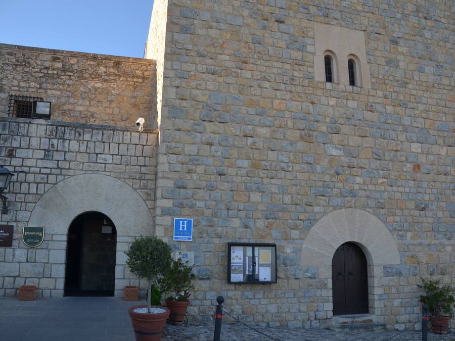 Un edificio de piedra con un gran arco de entrada, un ventanal arqueado más pequeño y un letrero que indica un hotel.