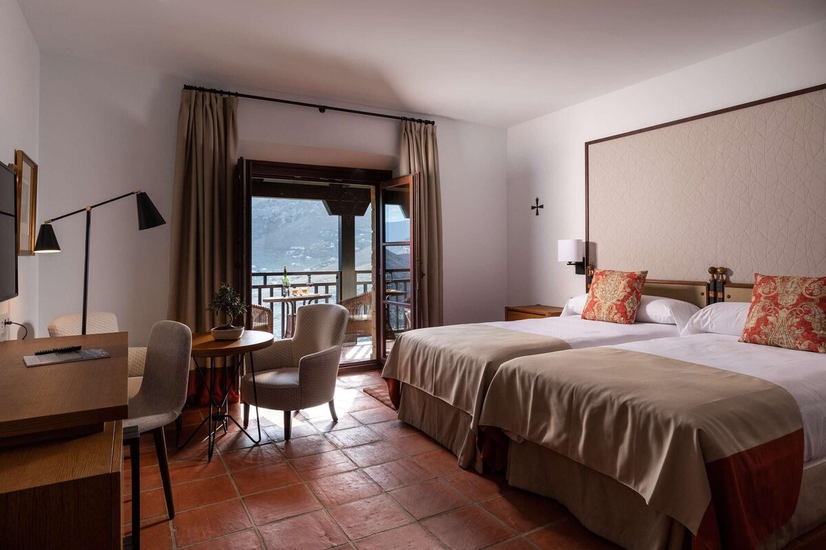 Habitación de hotel con cama, escritorio, silla, mesa y vistas al exterior.