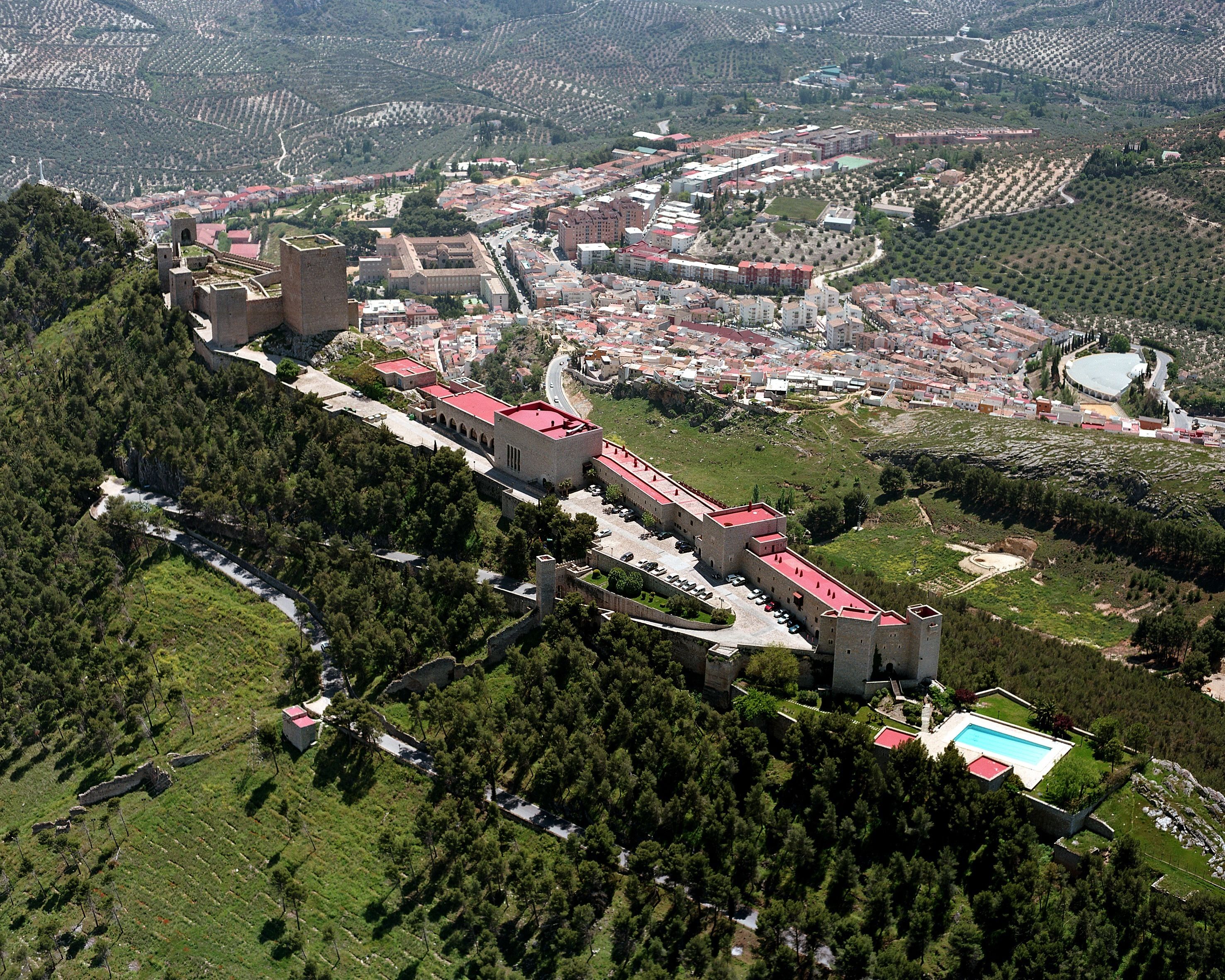 Una vista aerea di un complesso castellano storico con un fossato, circondato da fitti boschi e un piccolo villaggio.