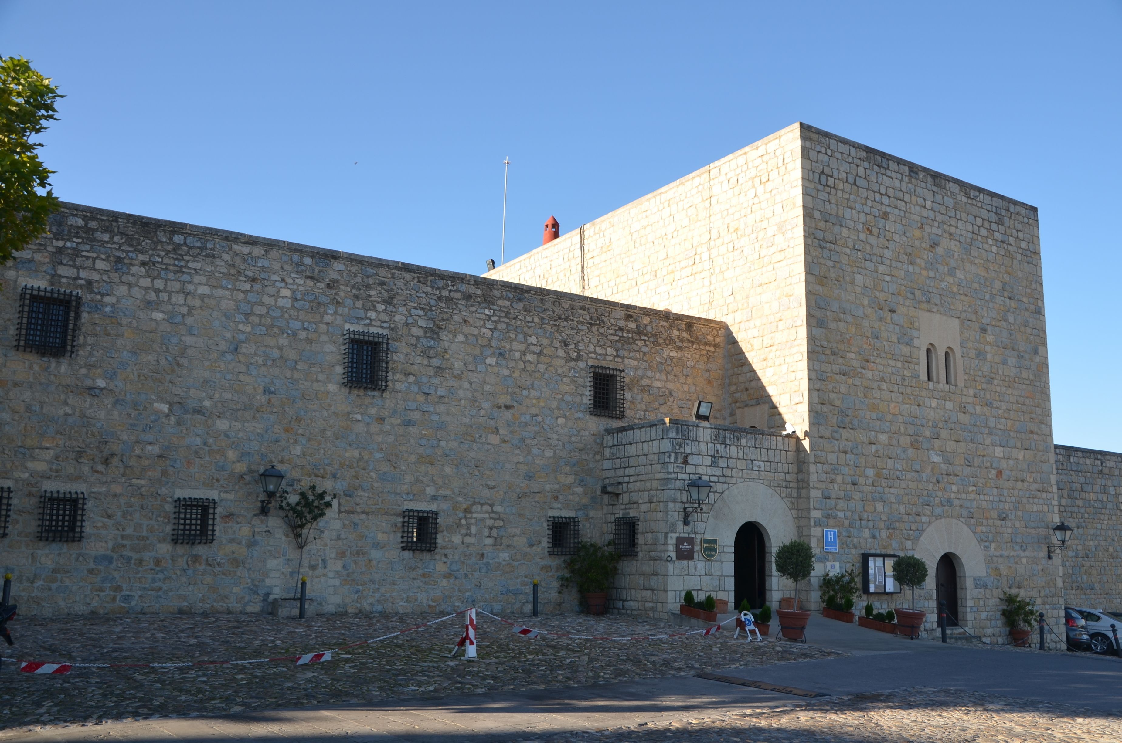 A stone building with a prominent tower, arched entrances, and potted plants.