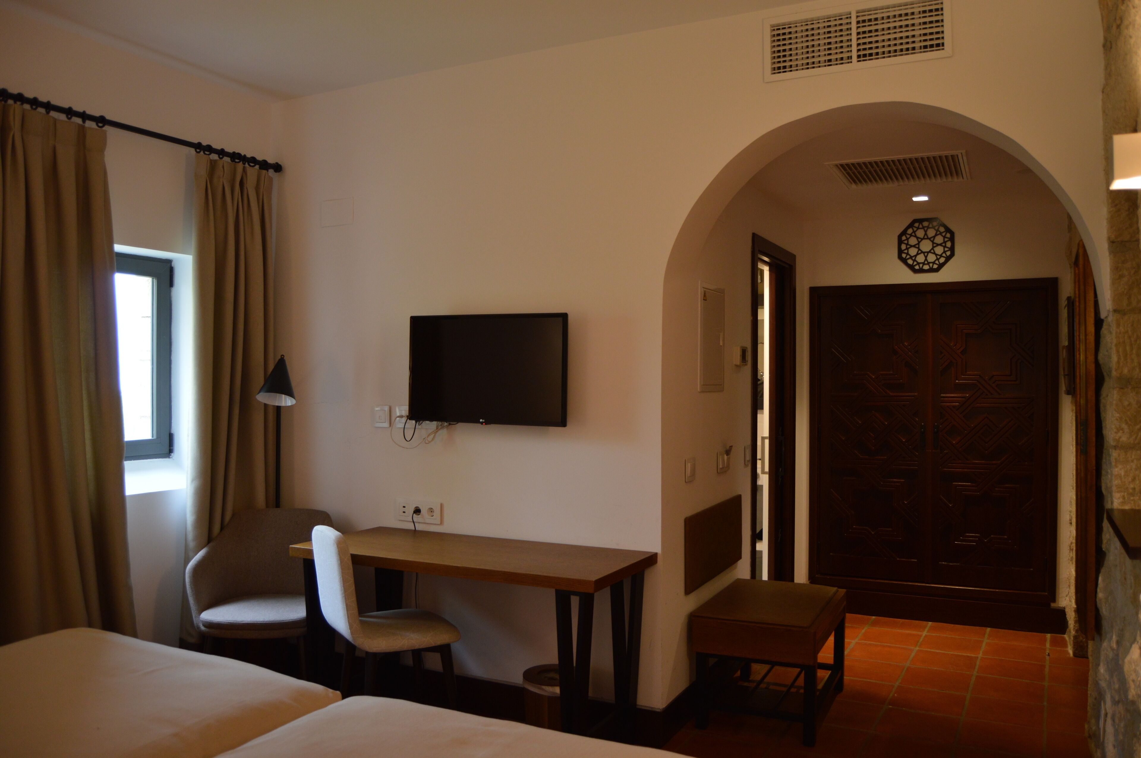 Une chambre d’hôtel équipée d’un lit, d’un bureau, d’une chaise, d’une télévision et d’une porte ornée d’un panneau décoratif.