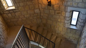Un escalier en pierre avec une rampe métallique, un luminaire fixé au mur et une petite fenêtre.