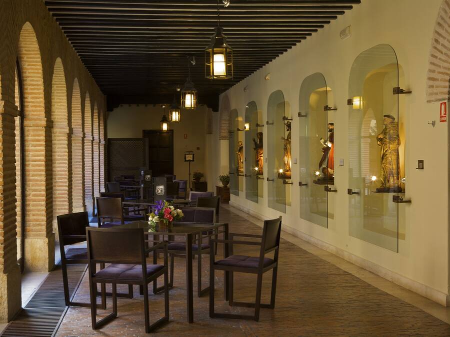A corridor with arched brick walls, a central seating area with tables and chairs, and hanging lantern-style lights.