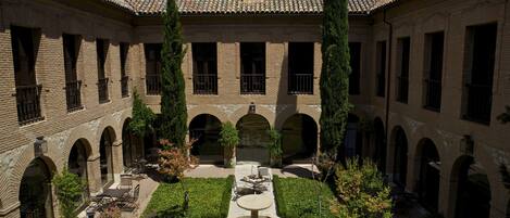 Un patio con una fuente, rodeado de edificios de ladrillo con ventanas de arco y techo de tejas.