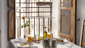 Mesa de desayuno preparada con platos, vasos y una jarrón, con vista a un edificio desde la ventana.