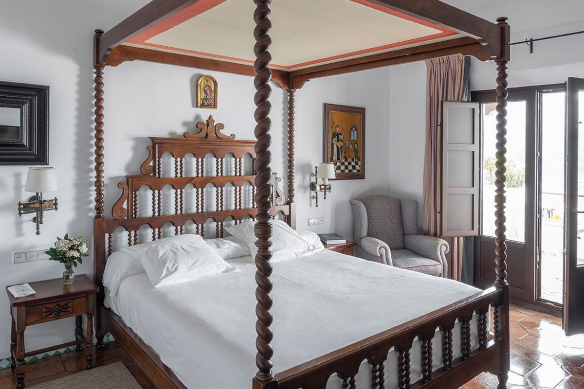 Een hemelbed met baldakijn, een nachtkastje, een stoel en een schilderij aan de muur.