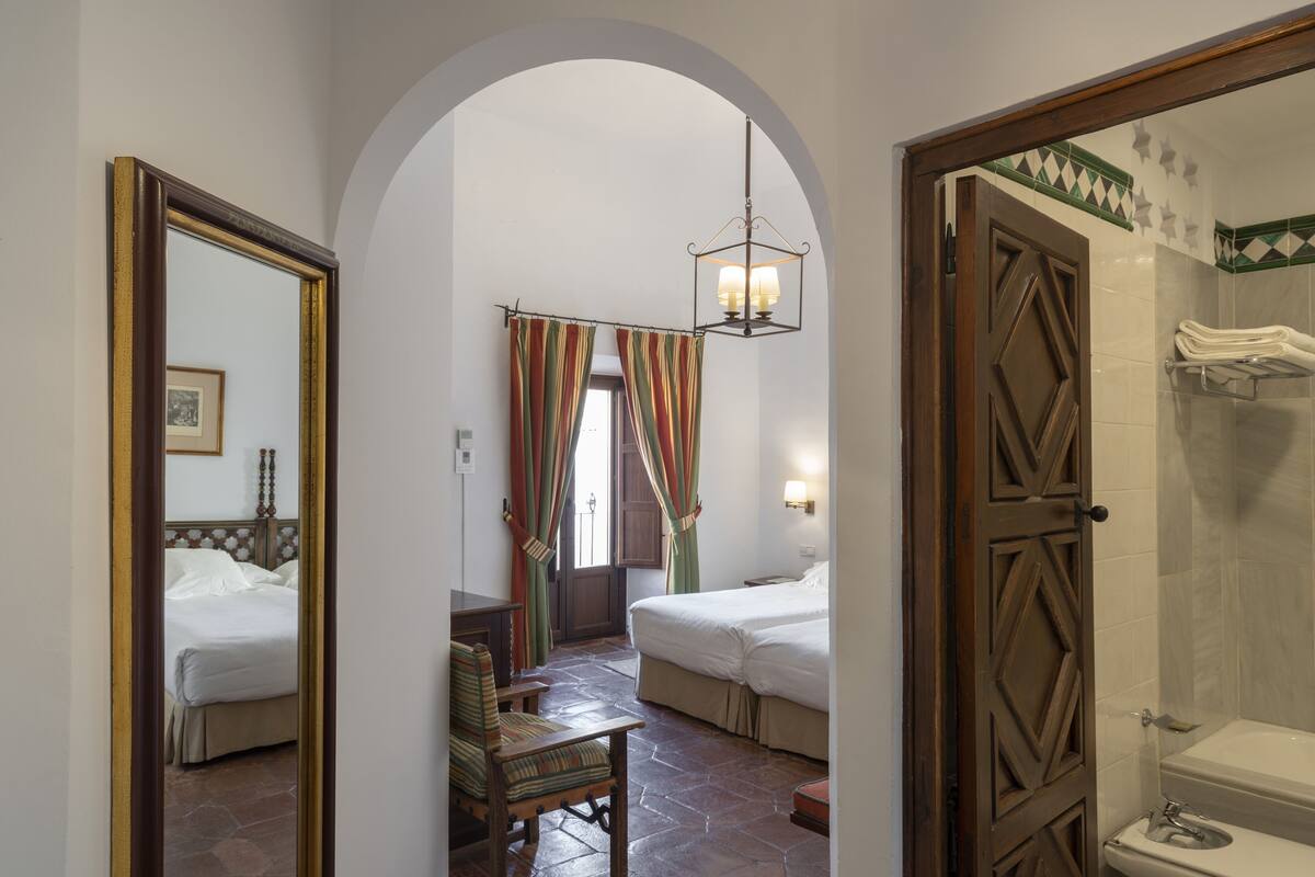 Une chambre d’hôtel comprenant un lit, une chaise, un miroir, une porte donnant sur une salle de bain et un espace douche.