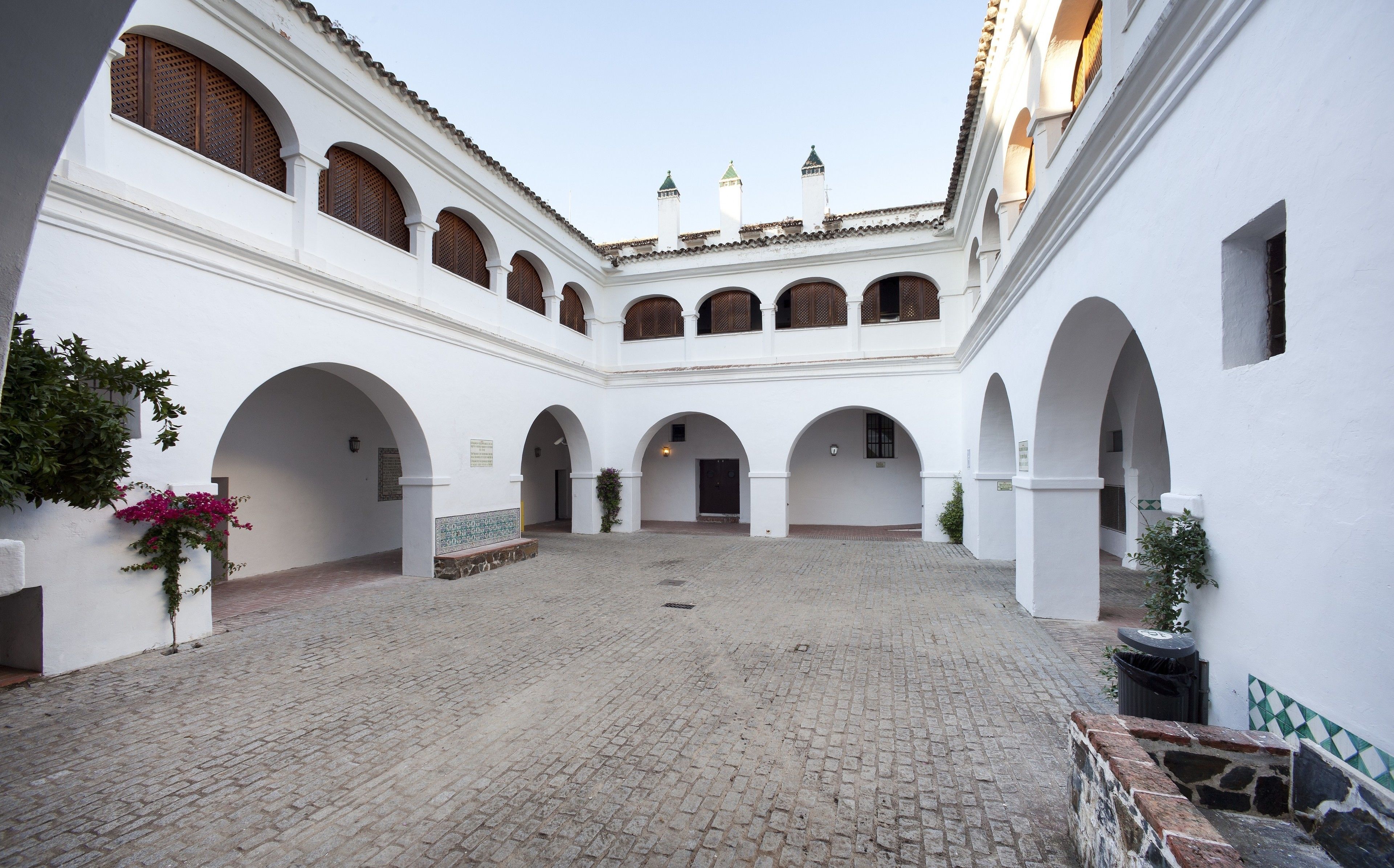 Une cour avec des murs blancs, de nombreuses arcades et un sol pavé de pierres.