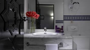 A bathroom with a white sink, mirror, and toilet. There is a towel hanging on the wall and a vase with red flowers on the counter.